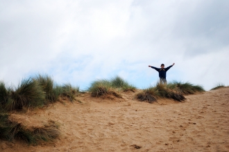 A little boy at Beach School standing triumphantly on top of a sand dune