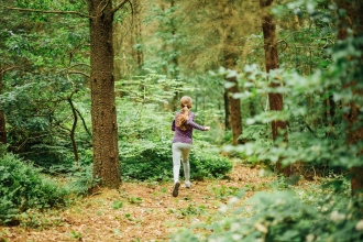 A teenager running through an autumnal pine woodland