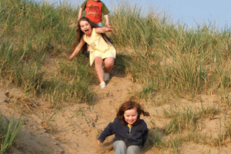 Children sliding down the sand dunes at Beach School in Lancashire