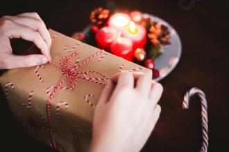 Person wrapping a Christmas present with brown paper and string