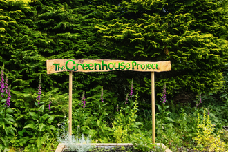 A wooden handpainted sign saying 'The Greenhouse project'