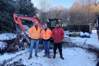 Three people in the snow standing in front of a digger