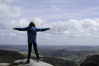 A woman standing on top of a rock with her arms outstretched
