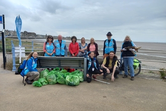 A group of smiling people with a large pile of rubbish collected from a beach