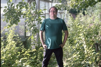 A man in a green t-shirt standing in front of a greenhouse