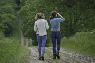 Two women walking down a country lane and looking through binoculars