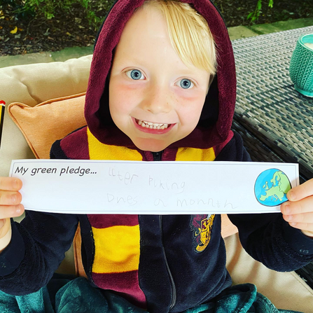 A child holding up a piece of paper that says 'My green pledge...'
