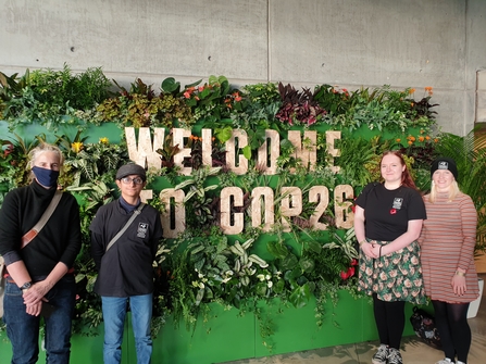 The Lancashire Wildlife Trust Youth Council standing in front of a sign surrounded by leaves that says, 'Welcome to COP26'
