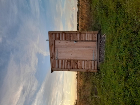 The front of a small wooden building holding a compost toilet at Lunt Meadows