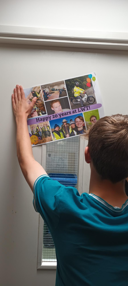 Lewis putting up posters on a door for Simon Work anniversary