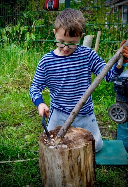 A child enjoying forest school with tools on a tree stump
