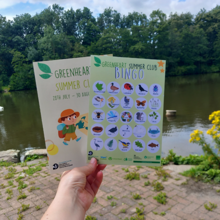 Nature bingo activity sheets held up against a beautiful river