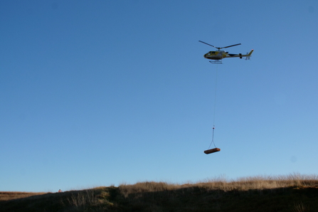A helicopter carrying materials for peatland restoration on Darwen Moor.