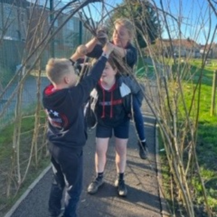 A group of children in a group underneath their handmade willow archway