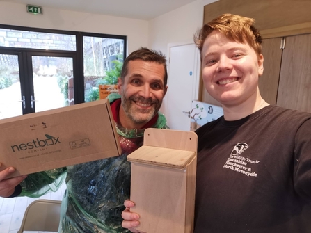 Two smiling volunteers holding nestboxes