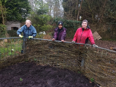 Volunteers standing by a woven willow fence