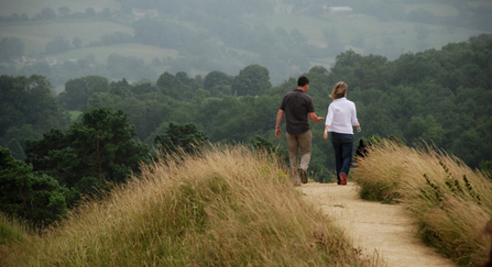 A couple walking along a gravel footpath, away from camera, towards distant trees and hills