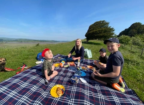 A young woman and her three sons having a picnic on a grassy hillside overlooking an estuary