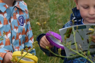Two children minibeast hunting in the grass with an ID guide and magnifying glasses