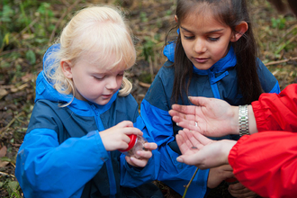 Two young children looking at an insect in a bug pot in the woods