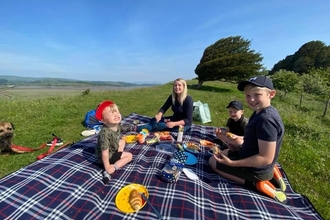 A young woman and her three sons having a picnic on a grassy hillside overlooking an estuary