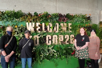 The Lancashire Wildlife Trust Youth Council standing in front of a sign surrounded by leaves that says, 'Welcome to COP26'
