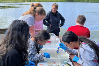 A group engaging in a seed bombing activity at the water's edge on a sunny day
