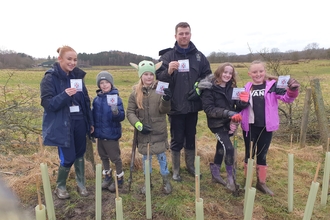 School children and their teacher standing with a row of planted trees