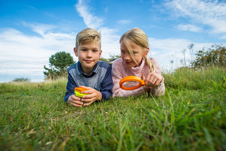 Children laying on grass with magnifying glass with blue sky 