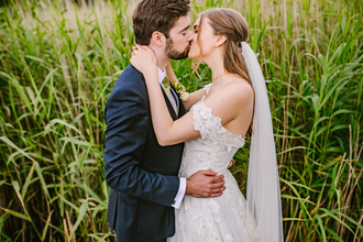 A bride and groom kiss whilst stood in front of reedbeds