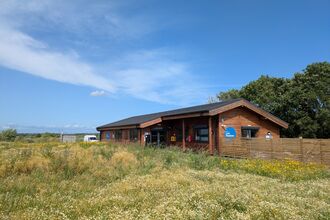 The Learning Centre, a wooden single storey building with a wildflower meadow in front and a fence. There is a blue sky above.