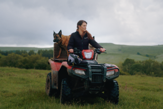 A woman is riding a quad bike with a german shepherd on the back