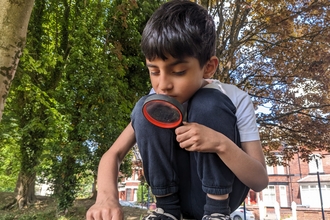 Boy crouching down looking through a magnifying glass