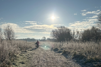 A person walks a dog along a frosty path in winter with a sunny clear blue sky