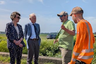 Four people standing on a farm, one holding a bulrush stem
