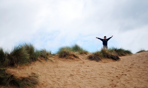 A little boy at Beach School standing triumphantly on top of a sand dune