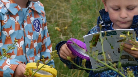 Two children minibeast hunting in the grass with an ID guide and magnifying glasses