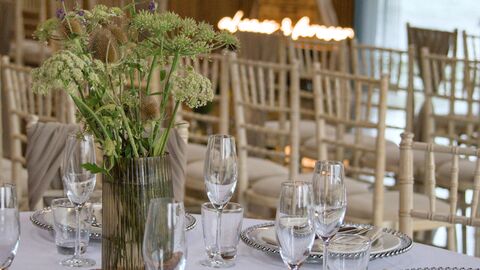 A close up of a table set ready for a wedding with rows of seats in the background