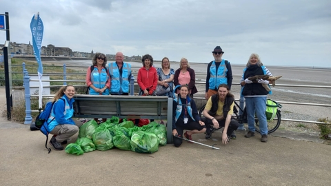 A group of smiling people with a large pile of rubbish collected from a beach