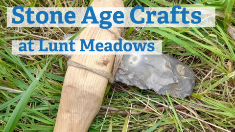 A middle stone age hand axe made from flint rock with a wooden handle and nettle string lies in the grass. Blue text over the top of the image says stone age crafts at lunt meadows