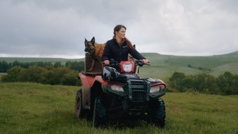 A woman is riding a quad bike with a german shepherd on the back