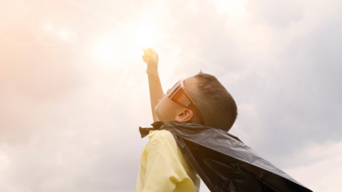 Child with a cape on in a superhero pose