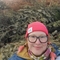 A woman wearing a hat in front of a pile of Christmas Trees
