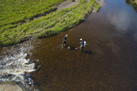 Two scientists standing in a river and measuring water quality