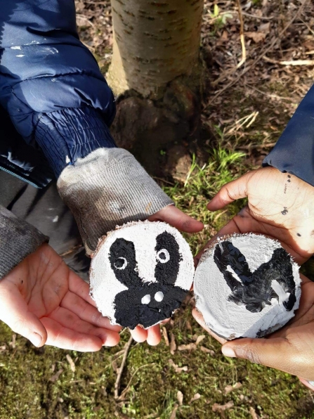 Two Forest School class members holding stones they've painted to look like badgers