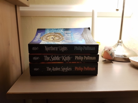 The His Dark Materials book trilogy stacked on a bedside table