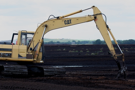 Yellow digger extracts black peat against desolate background