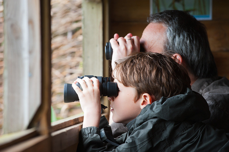 A man and a young boy looking out of a window with binoculars