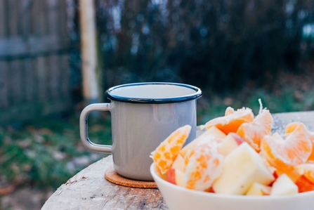 A bowl of orange segments and enamel mug on a table in a garden