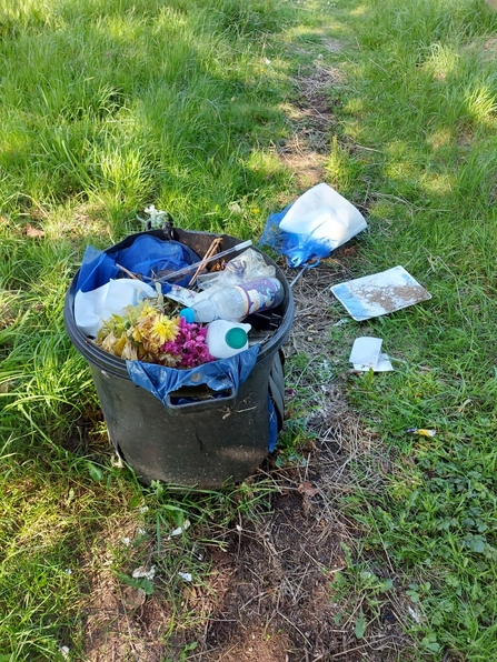 A black bin on a patch of grass, full of litter